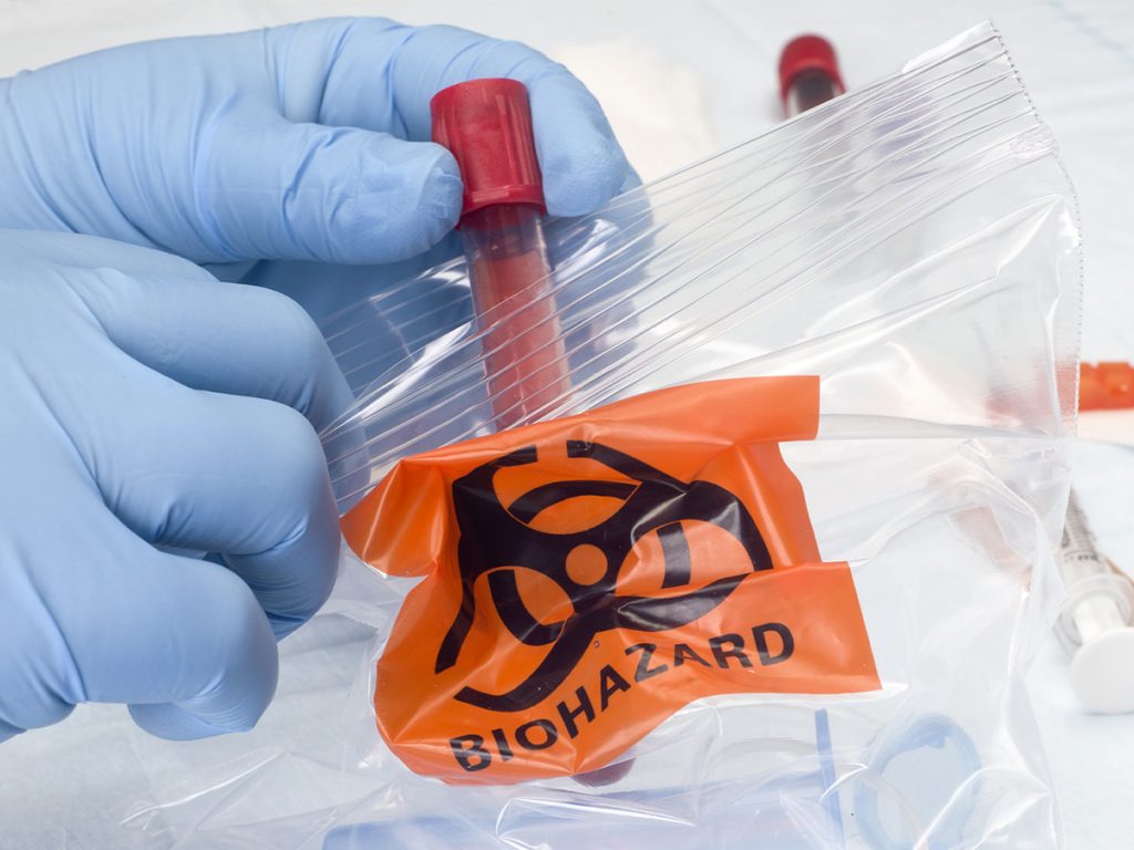 Nurse places blood collection tube and other medical waste into biohazard disposal bag.